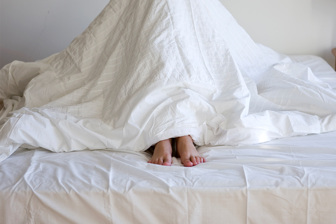 Person unter einer Bettdecke Person unter einer Bettdecke