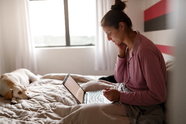 Frau sitzt auf ihrem Bett und arbeitet am Laptop