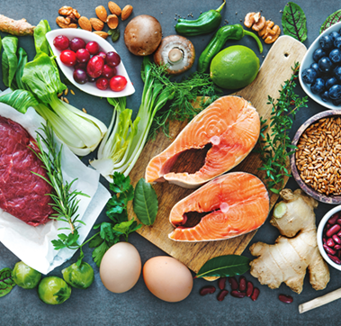 Auf einer Arbeitsfläche liegt zusammen drapiert eine Auswahl an Gemüse, Obst, Nüssen, Eiern, Fisch und Fleisch.