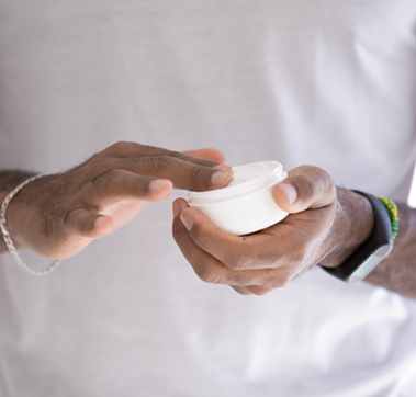 Ein Mann hält einen Tiegel in einer Hand und holt mit der anderen Hand etwas Creme heraus.